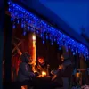 Three people sitting around a table outdoors at night, illuminated by blue icicle lights and a candle. Produktbild-Vorschau