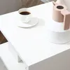 A white side table with a cup of coffee and a pink kettle on top. Produktbild-Vorschau