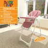 A pink baby high chair is shown in a room with a window and a rug. Produktbild-Vorschau