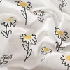 A close-up view of white fabric with a repeating pattern of black-outlined daisies with yellow centers. Produktbild-Vorschau