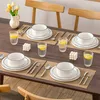 A dining table set for a meal with plates, bowls, glasses of water with lemon, cutlery, and a vase of flowers. Voir les images du produit