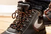 Close-up of a black work boot with orange laces and stitching, showing the brand logo. Náhľad obrázku produktu