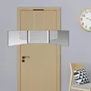A tri-fold mirror with LED lights hangs on a wooden door, with a chair and pillow visible to the right and a clock on the wall. Produktbild-Vorschau