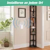 A white WiFi repeater is mounted on a wall next to a tall, narrow black bookshelf filled with books and decorative items. A large plant is in the foreground to the left, and a window is visible behind it. Produktbild-Vorschau