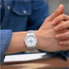 A close-up shot of a person's wrist wearing a silver watch. Produktbild-Vorschau