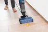 A person is using a wet and dry vacuum cleaner to clean up a spilled egg on a wooden floor. Podgląd zdjęcia produktu