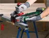A person is using a cordless angle grinder to cut a metal bar supported by sawhorses. Produktbild-Vorschau