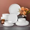 A collection of white porcelain dishes, a candle, and a floral arrangement are displayed on a table against a brown background. Náhled obrázku produktu