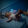A baby is being changed on a changing table at night, with a night light cube nearby. Voir les images du produit