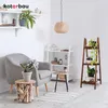 A cozy living room corner with a gray armchair, a wooden plant stand, and shelves filled with plants and decor. Produktbild-Vorschau