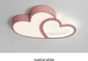 A pink cloud-shaped ceiling light with two heart shapes inside, illuminated with neutral white light, mounted on a light gray ceiling. Náhled obrázku produktu