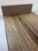 A close-up view of a wood-like flooring sample with a textured surface and a raised edge. Produktbild-Vorschau