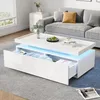 A modern living room scene featuring a white high-gloss coffee table with LED lighting and open drawers, placed on a gray rug in front of a gray sofa. Voir les images du produit