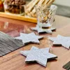 Star-shaped coasters are arranged on a wooden table, with a glass and snacks in the background. Produktbild-Vorschau