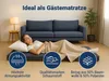 A woman is lying on a folded mattress in front of a sofa, with a blanket covering her. There are informational icons and text overlays. Produktbild-Vorschau
