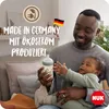 A father is holding his baby and a baby bottle. The text indicates the product is made in Germany with eco-friendly electricity. Produktbild-Vorschau