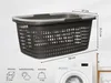 A dark grey laundry basket with dimensions indicated, placed in front of a washing machine and a wooden towel rack. Produktbild-Vorschau
