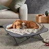 A golden retriever dog is sleeping on a raised dog bed with a blanket and a stuffed toy. Produktbild-Vorschau