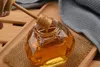 A glass jar of honey with a honey dipper, placed on a wooden tray with a textured cloth. Náhled obrázku produktu