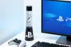 A PlayStation-themed lava lamp sits on a desk next to a computer monitor and a game controller. Podgląd zdjęcia produktu