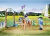 A Playmobil set depicting a modern riding school with figures, a horse, and accessories, set against a backdrop of a waterfall and landscape. Produktbild-Vorschau