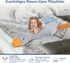A young girl is lying on a large plush goose toy on a bed. Náhľad obrázku produktu
