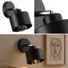 A collage of images showing a black wall lamp with a clear bulb, and a framed abstract line drawing of a face. Produktbild-Vorschau