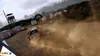 A rally car kicking up dust on a dirt track, with trees and a watchtower in the background. Produktbild-Vorschau