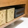 Two woven baskets and a black plastic storage box with a lid are placed on a wooden shelf. Anteprima dell’immagine prodotto