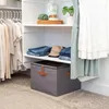 A closet interior with clothing on hangers, folded clothes on shelves, and a storage bin on the floor. Náhled obrázku produktu