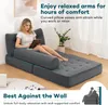 A woman is sitting on a sofa bed, using a tablet. The sofa bed is in a living room setting with a plant and a window in the background. Náhled obrázku produktu