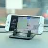 A smartphone is mounted on a car dashboard using a black silicone phone holder, displaying a navigation app. Produktbild-Vorschau