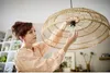 A woman is changing a light bulb in a rattan pendant lamp. Produktbild-Vorschau
