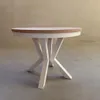 A round dining table with a white base and a light wood tabletop, set against a neutral wall and concrete floor. Voir les images du produit