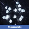 String lights wrapped around a tree trunk at night with rain falling. Produktbild-Vorschau