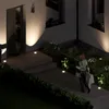 A woman walks up a path at night, illuminated by ground lights, carrying shopping bags. Produktbild-Vorschau