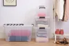 Storage boxes filled with folded clothes are arranged on a floor next to a clothing rack. Produktbild-Vorschau