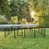 A black metal dog playpen is set up on a green lawn in a garden with trees and flowers in the background. Produktbild-Vorschau