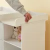 A person's hand is shown adjusting the edge of a white changing table with shelves below containing stuffed animals. Podgląd zdjęcia produktu