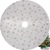 A white circular Christmas tree skirt with silver snowflake patterns is shown, with a portion of a decorated Christmas tree visible in the bottom right corner. Náhled obrázku produktu