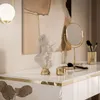A close-up of a white console table with gold accents, featuring decorative items like a bust, a makeup mirror, and brushes. Produktbild-Vorschau