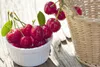Cherries in a white bowl next to a basket on a wooden surface. Anteprima dell’immagine prodotto