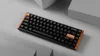 A black mechanical keyboard with a wooden accent is placed on a light gray surface with geometric shapes in the background. Produktbild-Vorschau