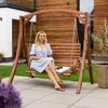 A woman sits on a wooden swing in a garden setting. Náhled obrázku produktu