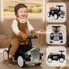 A baby is riding a black retro ride-on car indoors. Náhled obrázku produktu