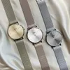 Three Cluse watches with mesh straps are laid out diagonally on a light-colored, textured fabric. Voir les images du produit
