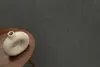 A beige donut-shaped vase sits on a wooden side table against a dark gray textured background. Produktbild-Vorschau
