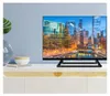 A television set is displayed on a white cabinet with a light blue wall in the background. Decorative items like a vase and a bowl are placed to the left of the TV. Podgląd zdjęcia produktu