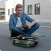 A young boy is sitting on the ground playing with a remote-controlled tank. Anteprima dell’immagine prodotto