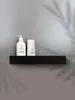 Two bottles of toiletries on a black shelf against a gray wall. Produktbild-Vorschau